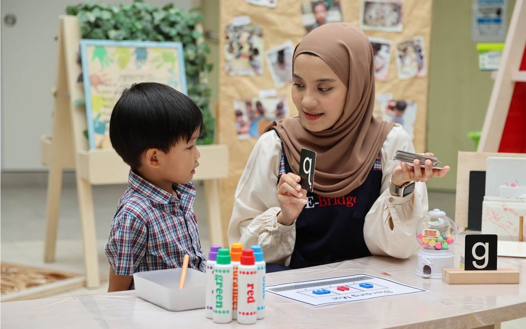 Teacher guiding child in phonics learning with letter flashcard at preschool
