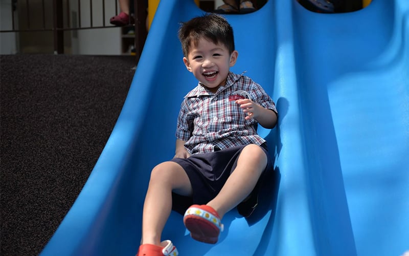E-Bridge preschooler happily playing on a blue slide outdoors