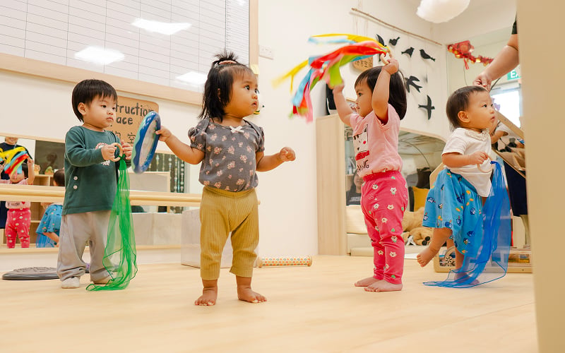 Toddlers playing with colorful ribbons during childcare activities at E-Bridge.