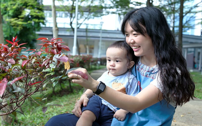 Preschool teacher and toddler exploring outdoor garden plants in Singapore.