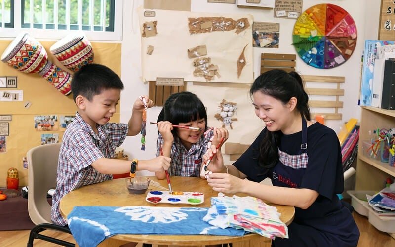 Preschool teacher guiding children in art painting activity in Singapore.