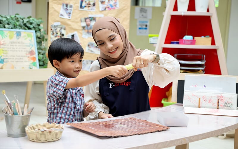 Teacher assisting young boy with hands-on learning activity at preschool.